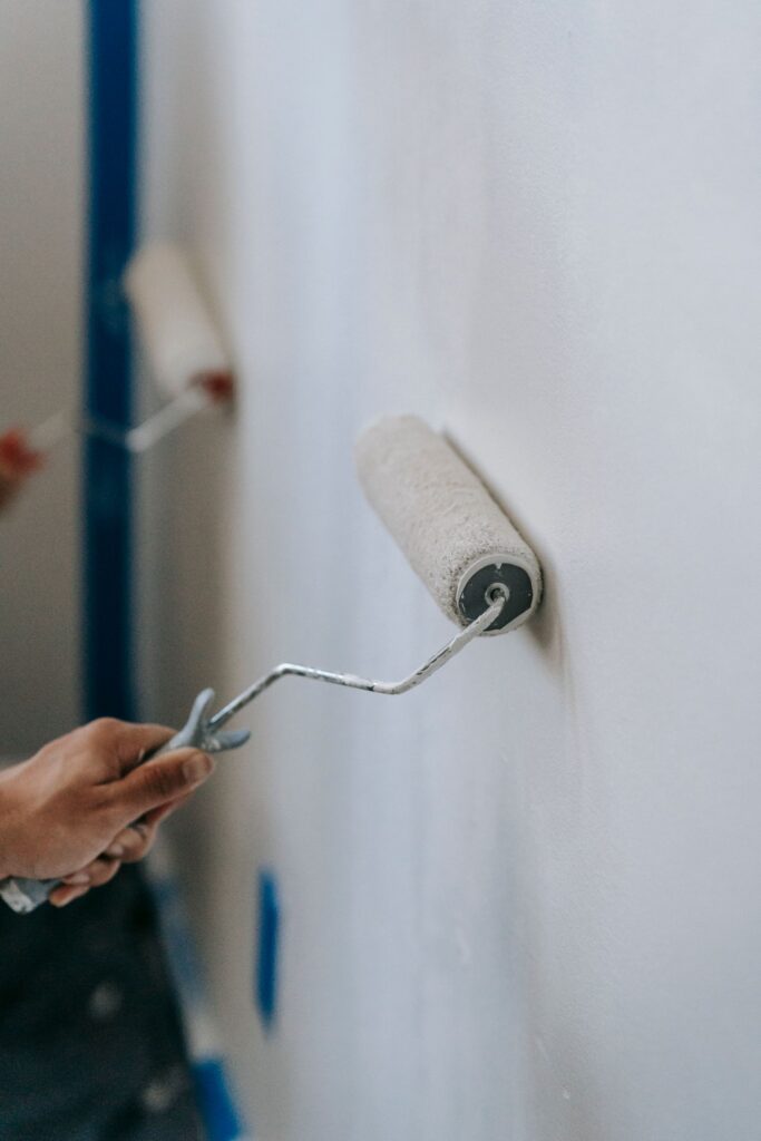 Hands using paint rollers on an interior wall during a renovation