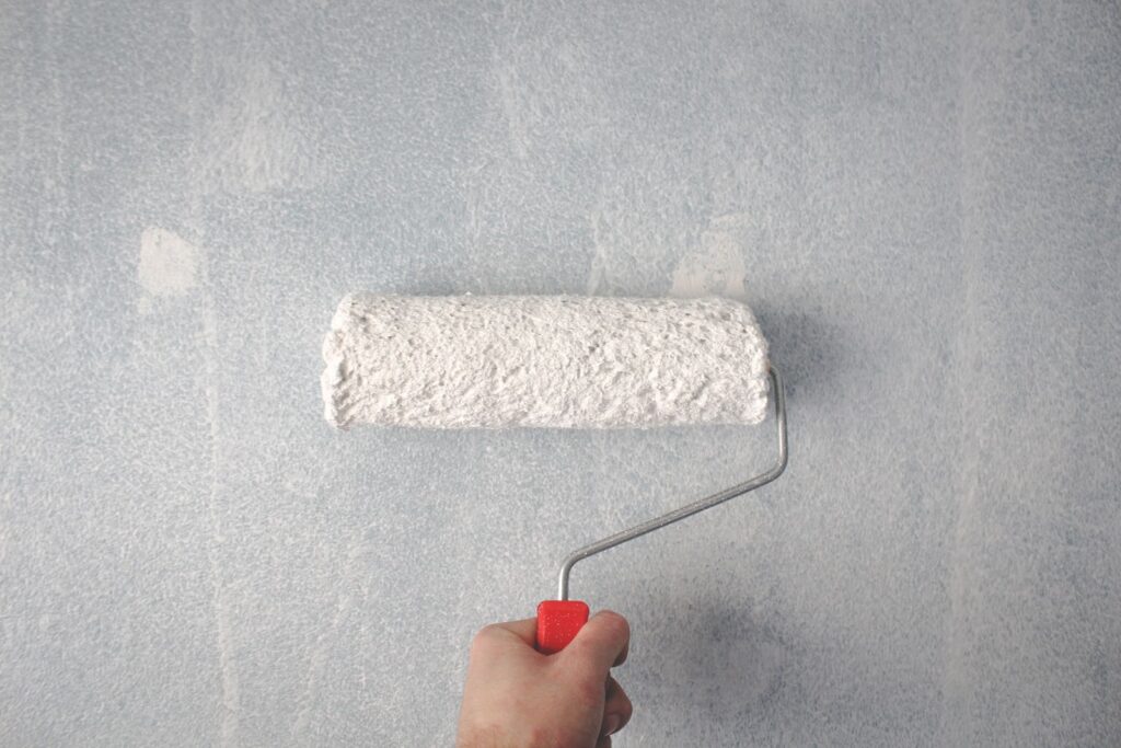 Close-up of a paint roller applying white paint to an interior wall